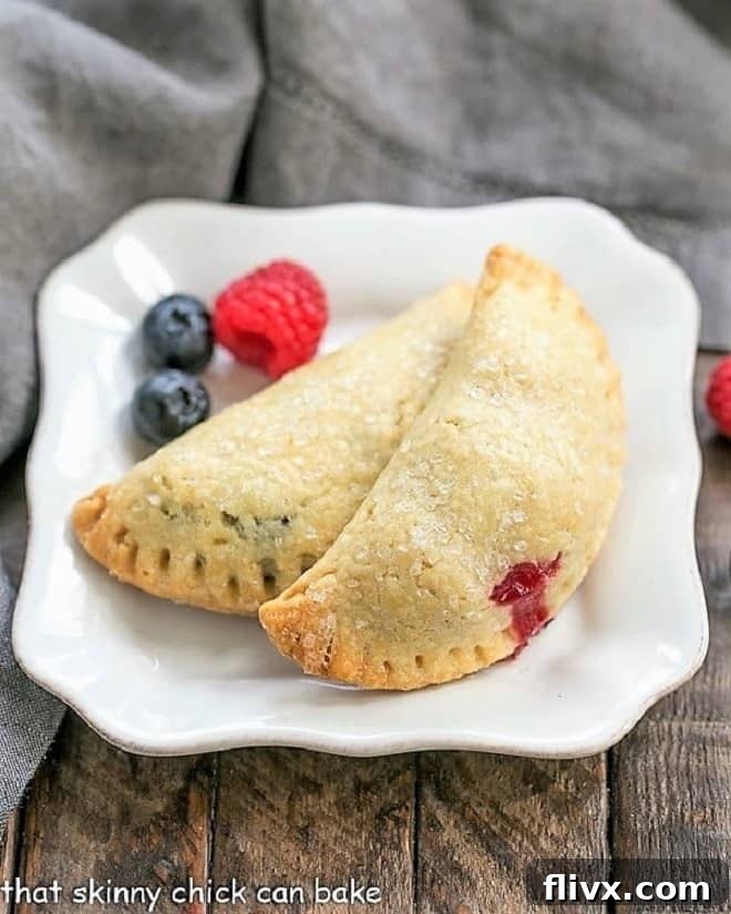 Rustic Berry Turnovers on a white plate with 3 berries, showcasing their golden crust and juicy filling.