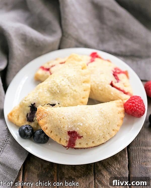 Rustic Berry Turnovers on a round white plate, highlighting their golden, flaky crusts and sweet berry filling.