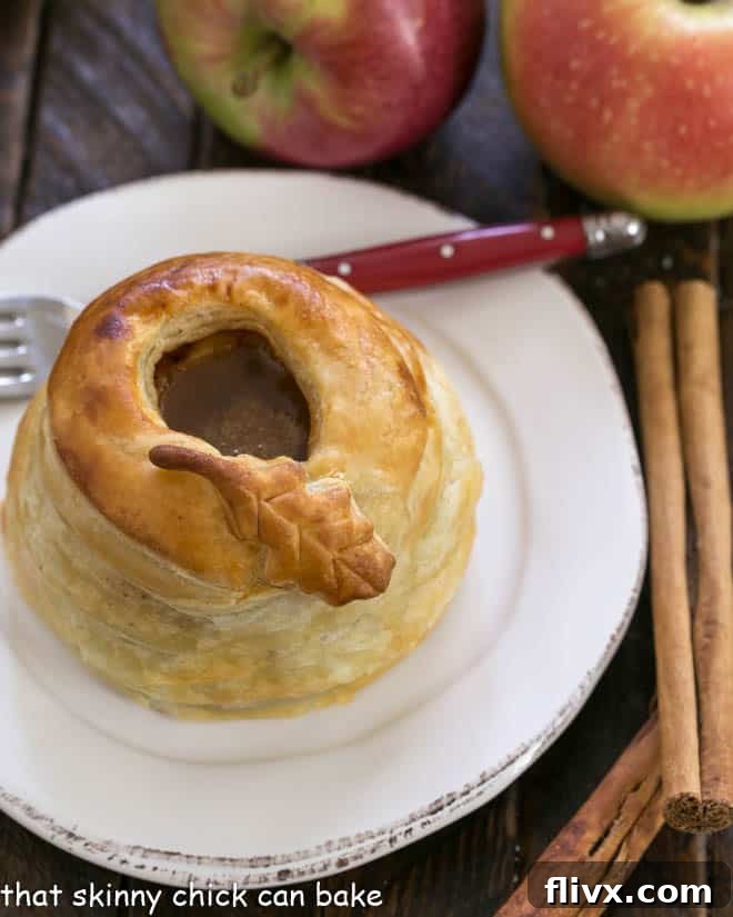 A beautifully golden-brown pastry wrapped caramel apple on a white plate, served with a red-handled fork.