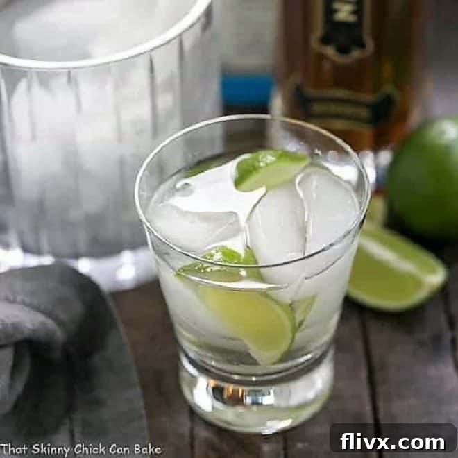 A vibrant St. Germain Gin and Tonic Cocktail in a short glass, adorned with fresh lime wedges and plenty of ice.