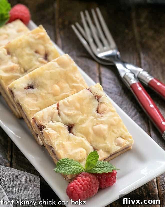 White chocolate raspberry bars on a white tray with fresh raspberries and mint sprigs as garnish.