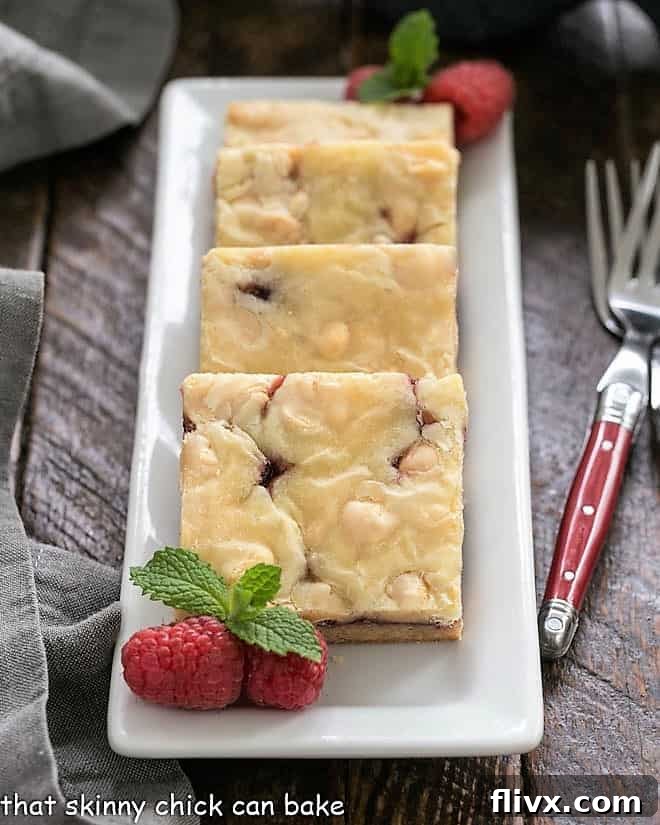 White Chocolate Raspberry Bars lined up on a rectangular white tray, showcasing their beautiful layers.