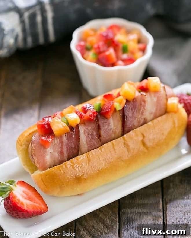 Delicious Bacon Wrapped Hot Dogs served with fresh Fruit Salsa on a narrow white ceramic plate, ready to be enjoyed.