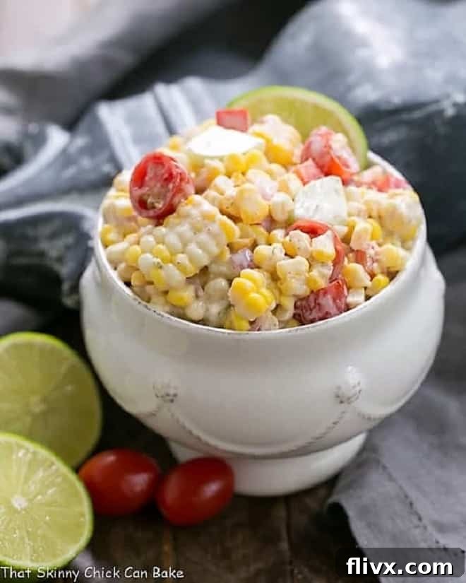 A beautiful white tureen filled with Spicy Mexican Street Corn Salad, garnished with fresh lime wedges and vibrant grape tomatoes.