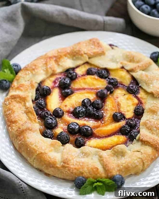A beautifully baked Peach Blueberry Galette presented on a pristine white serving plate, ready to be enjoyed. The golden, flaky crust perfectly cradles the juicy fruit filling.