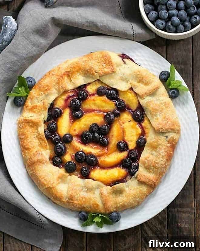 An inviting overhead view of a freshly baked Peach Blueberry Galette, showcasing its golden, crimped crust and vibrant fruit filling, presented on a round white plate.