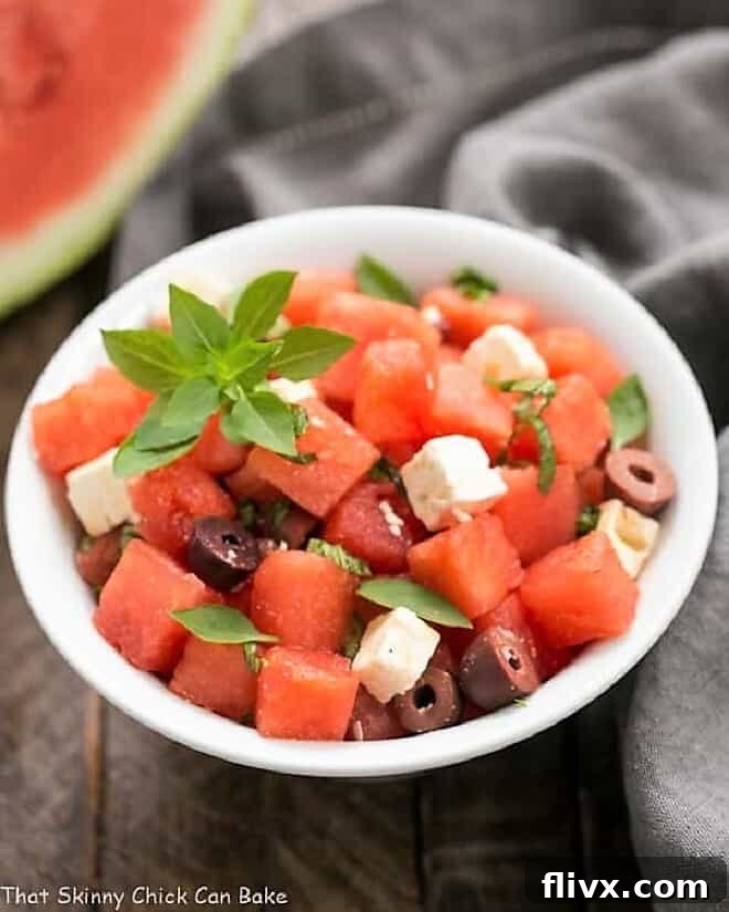 A close-up view of Watermelon Feta Basil Salad with Balsamic Vinaigrette in a pristine white bowl, showcasing vibrant red watermelon cubes, creamy white feta, green basil leaves, and dark kalamata olives.