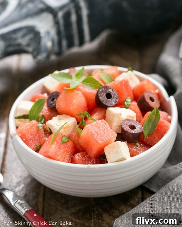 A close-up of Watermelon Feta Basil Salad with Balsamic Vinaigrette, elegantly presented in a white ceramic bowl, garnished with a sprig of fresh basil. A red-handled fork rests beside the bowl, ready for indulgence.
