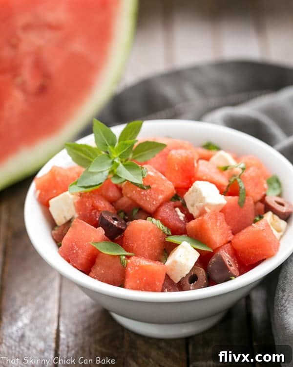 A vibrant close-up of Watermelon Feta Basil Salad with Balsamic Vinaigrette in a white bowl, beautifully garnished with fresh basil leaves. The focus is on the rich textures and colors of the ingredients.