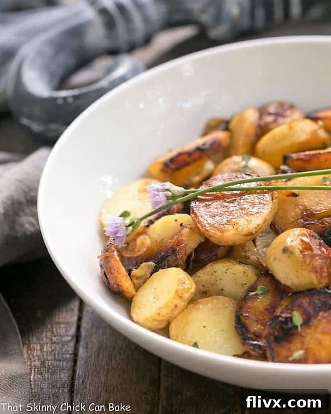 Grilled Potato Packets with Shallots and Thyme in a white serving bowl garnished with vibrant chive blossoms, ready to serve.
