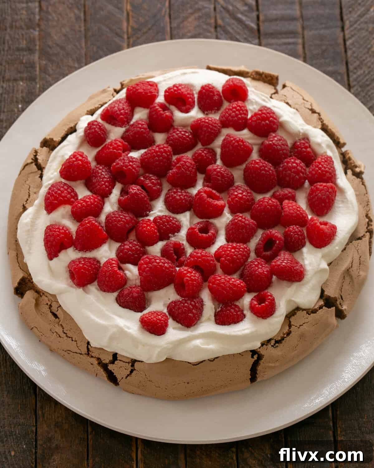 Cooled chocolate pavlova topped with sweetened whipped cream and fresh raspberries, ready for serving.