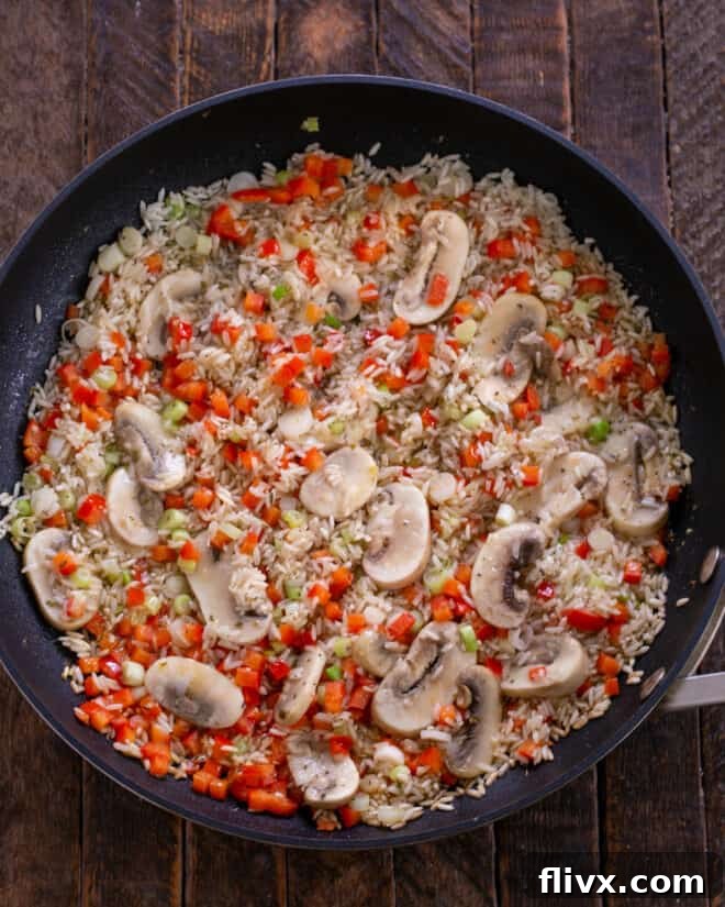 Rice and vegetables sautéing in a skillet until mushrooms are tender.