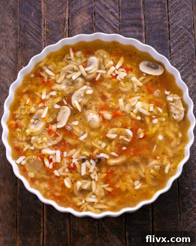 Chicken broth being poured over the rice mixture in a baking dish.