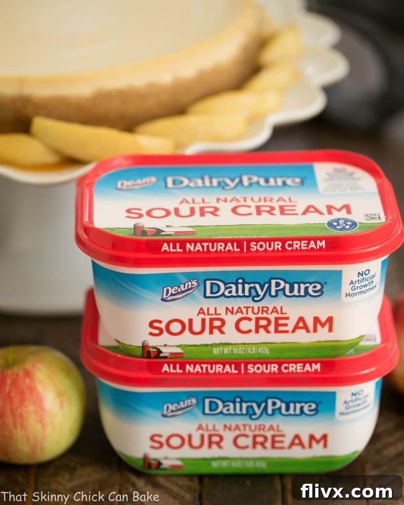 Two packages of high-quality DairyPure sour cream positioned in front of a beautifully baked Easy Sour Cream Cheesecake with Caramel Apples.