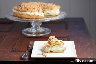 A delicate slice of Paris-Brest served on a white plate, with the rest of the pastry visible in the background