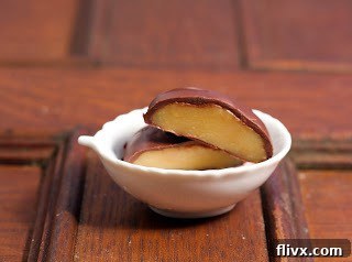 A luscious chocolate-covered caramel, expertly cut in half to reveal its soft, chewy center, resting in a small white bowl.