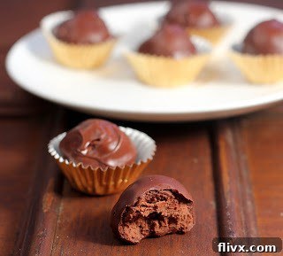 A perfectly crafted homemade chocolate truffle with a single bite removed, revealing its creamy interior, surrounded by other pristine truffles.