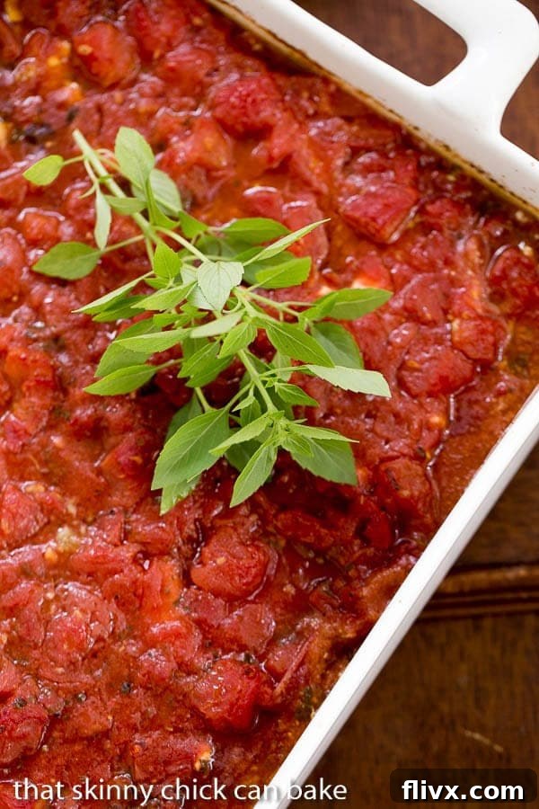A freshly baked Chicken Feta Casserole in a white ceramic dish, garnished with a sprig of green basil, ready to be served hot from the oven.
