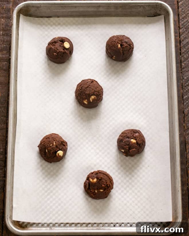 Rounds of cookie dough being scooped onto a parchment-lined baking sheet.