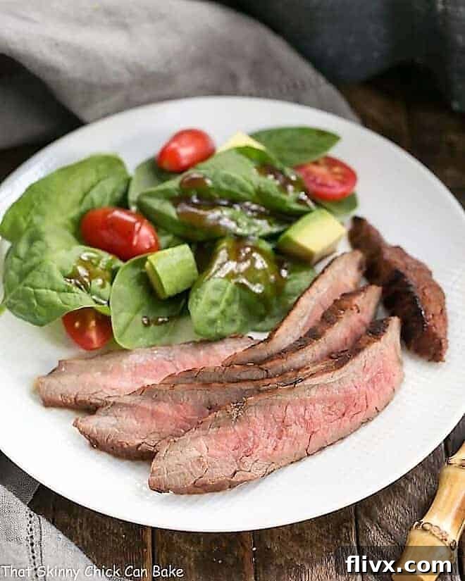 Red Wine, Soy, Balsamic Marinated Flank Steak on a white dinner plate with a spinach salad