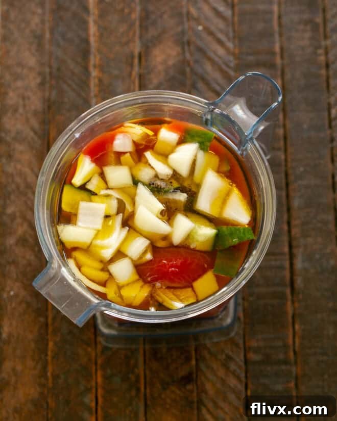 Fresh gazpacho ingredients being added to a blender.