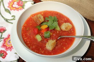 Gazpacho in a white bowl with toppings and a spoon.