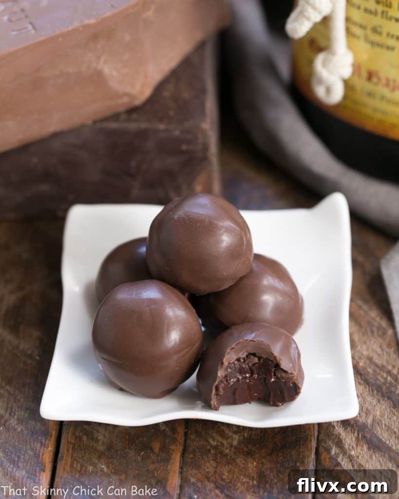 A close-up view of elegant Chocolate Frangelico Truffles arranged on a square white ceramic plate, showcasing their smooth, dark chocolate coating.