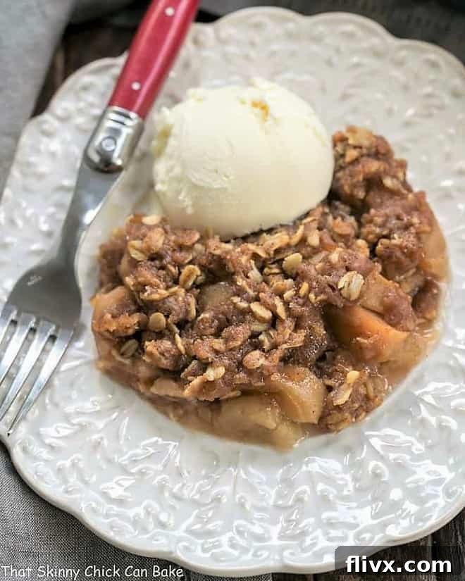 Easy Slow Cooker Apple Crisp with Oatmeal served on a decorative white plate with vanilla ice cream, garnished with a red handled fork.
