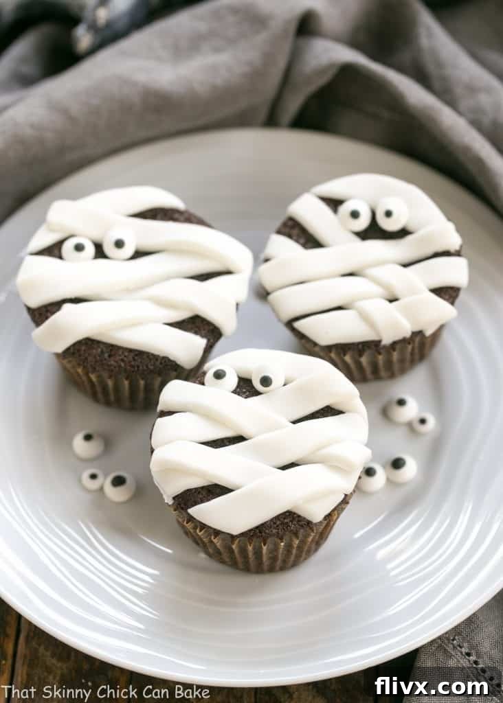 Delightful Chocolate Mummy Cupcakes adorned with sugar eyes, arranged on a round white ceramic plate for a festive Halloween treat.