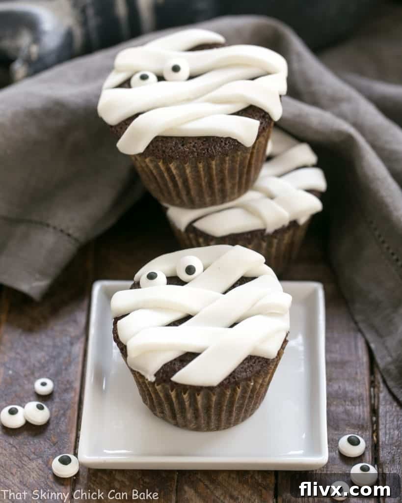 A playful stack of EASY Chocolate Mummy Cupcakes, each decorated with fondant strips and adorable sugar eyes, ready for Halloween.