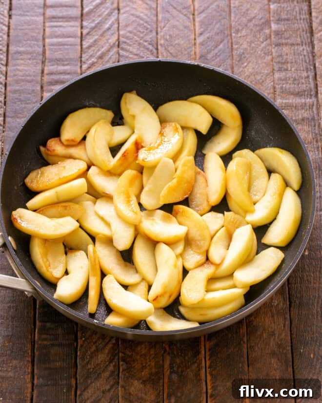 Sliced Granny Smith apples being sauteed in a pan with butter and sugar until tender.