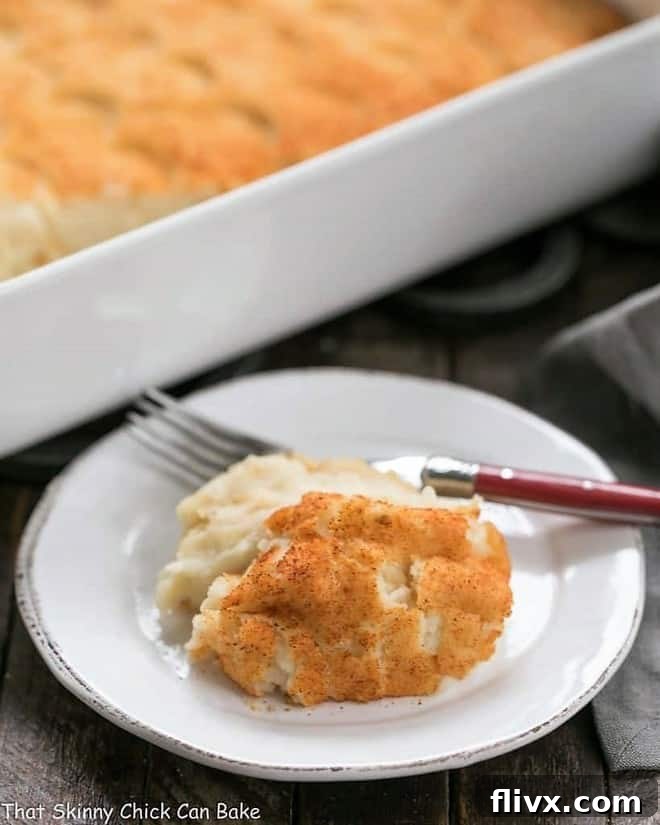 A serving of Easy Puffed Potatoes Casserole on a small white plate with a red handled fork, highlighting its creamy texture.
