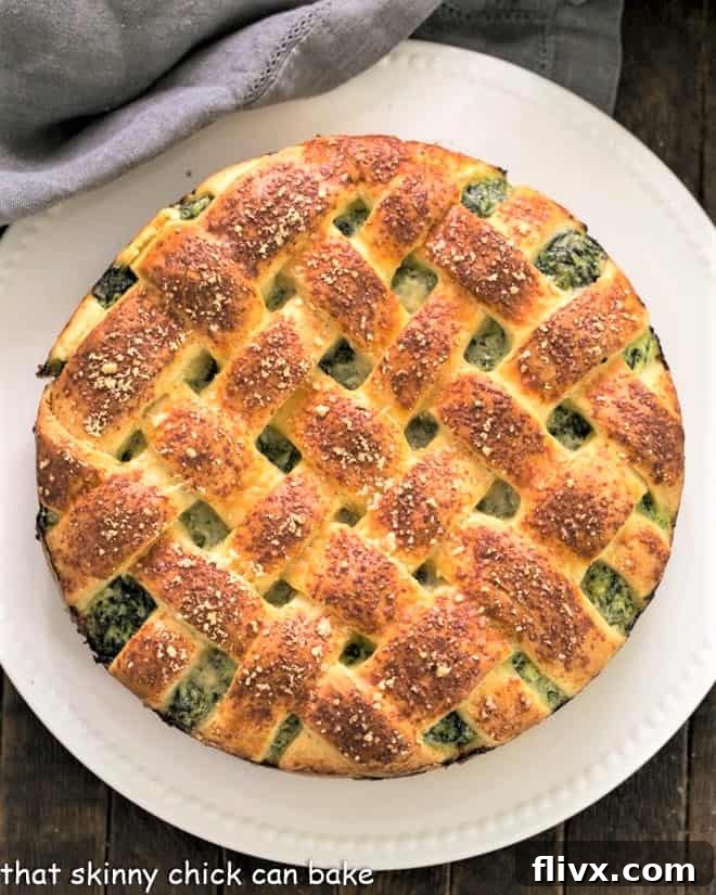 An overhead view of a perfectly baked Spinach Torta Rustica, showcasing its golden lattice crust and substantial form, presented on a round white serving plate.