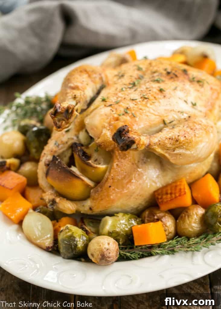 Oven roasted chicken with a mix of roasted fall vegetables on an oval serving platter, garnished with fresh herbs.