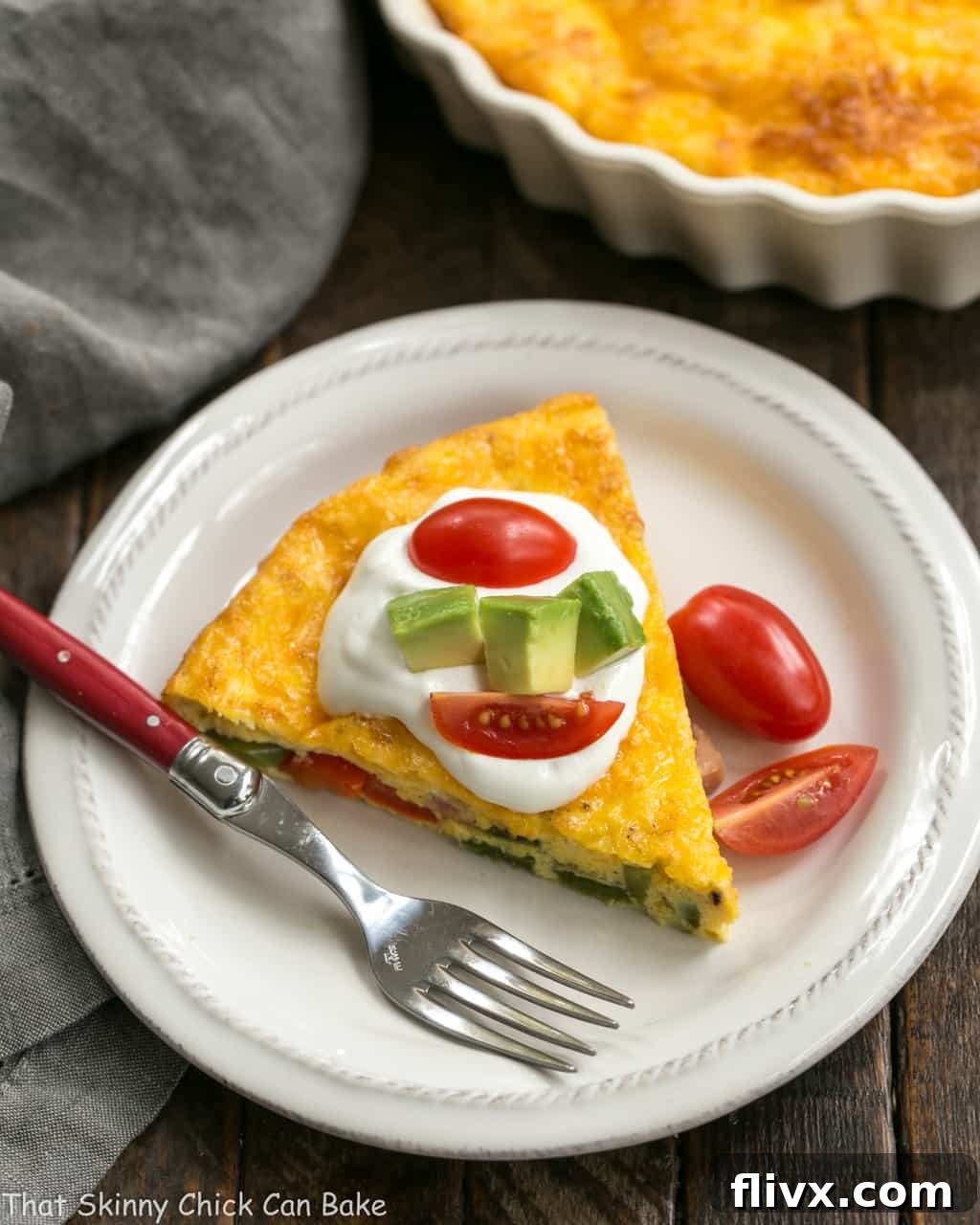 A perfectly sliced Baked Denver Omelet presented on a pristine white plate with a red-handled fork, revealing its fluffy texture and vibrant, colorful ingredients like ham, bell peppers, and cheese.