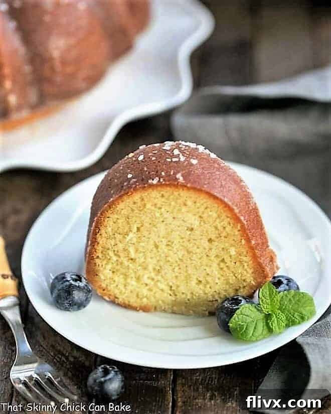 A beautifully sliced Kentucky Butter Bundt Cake on a white dessert plate, garnished with fresh blueberries and a delicate sprig of mint.