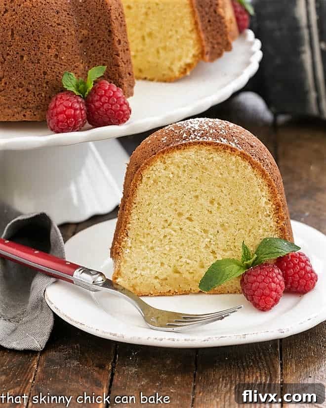 A perfectly sliced piece of moist white chocolate pound cake rests on a pristine white plate, garnished with vibrant red raspberries, showcasing its delicate texture.