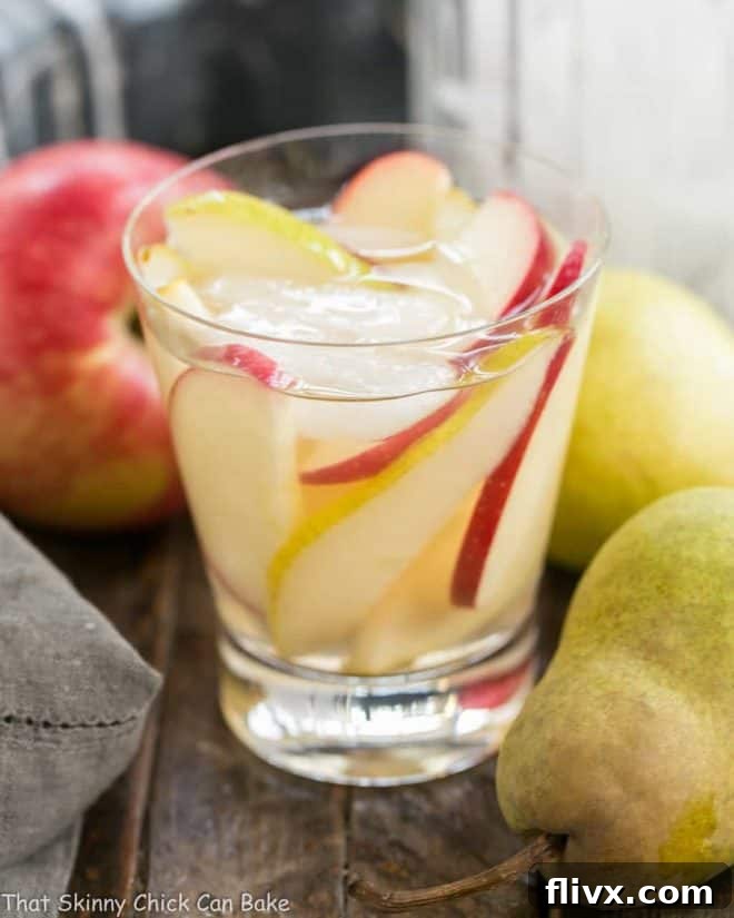 A refreshing glass of Apple Cider Sangria, garnished with apple and pear slices, and ice. Perfect for fall celebrations.