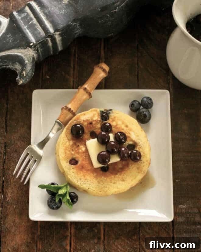 A stack of golden buttermilk pancakes topped with a generous drizzle of homemade blueberry maple syrup and fresh blueberries.
