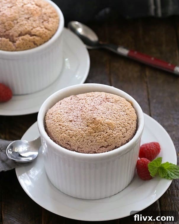 Two raspberry souffles on white dishes with spoons.