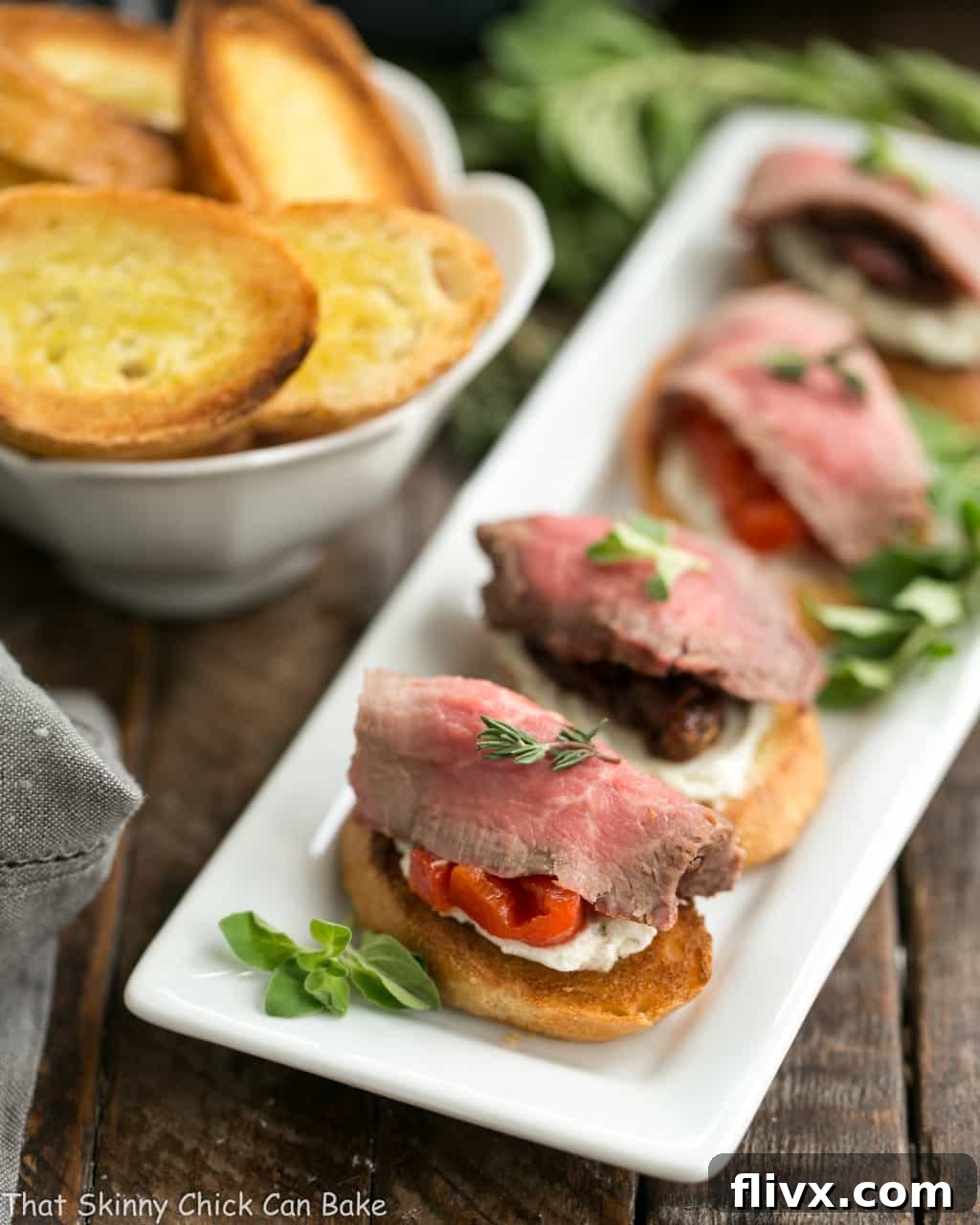 Rows of beautifully arranged Beef Crostini with Blue Cheese Spread on a long white platter, showcasing vibrant colors and textures, ready for guests.