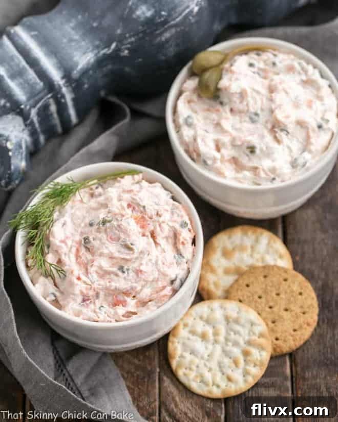 Two bowls of creamy smoked salmon dip with an assortment of crackers on the side.