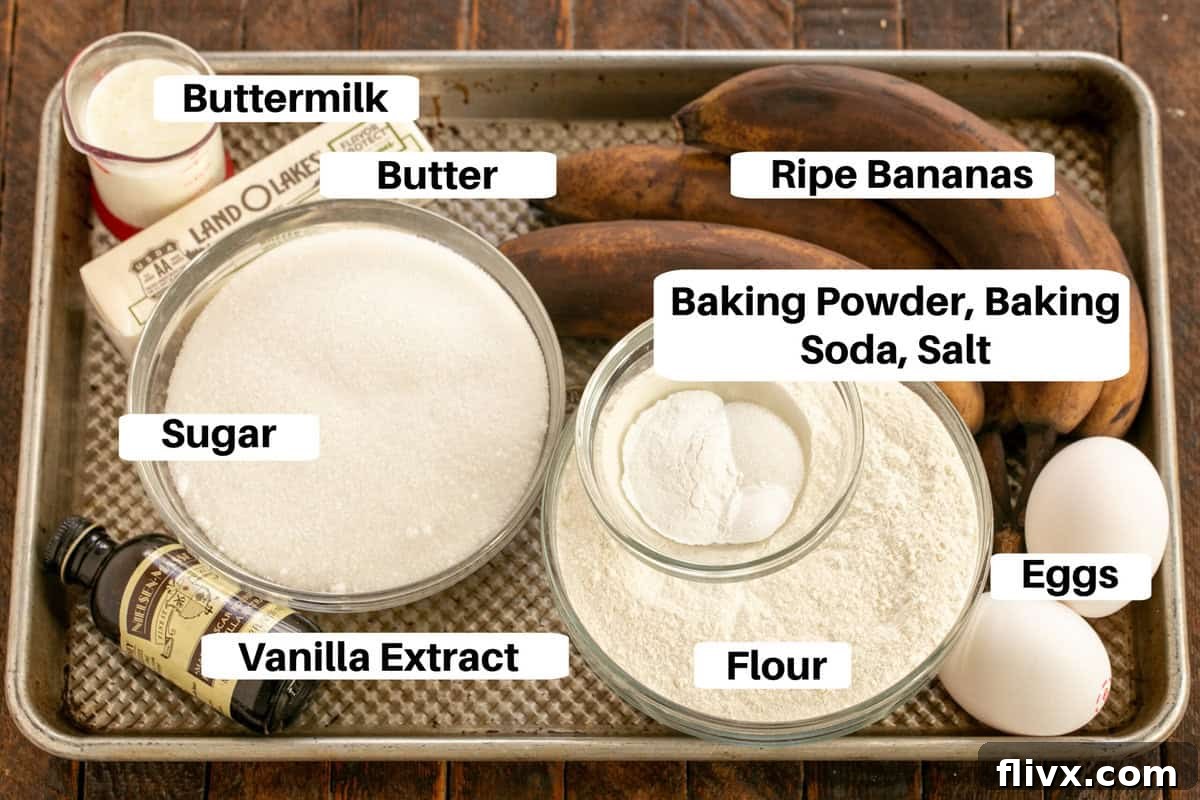 A collection of Buttermilk Banana Bread ingredients, including ripe bananas, butter, eggs, flour, sugar, and buttermilk, neatly arranged on a metal sheet pan with descriptive labels.