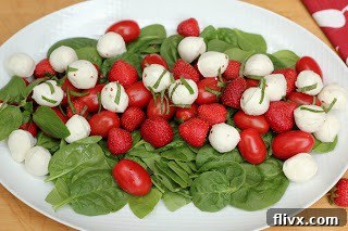 Close-up view of the fresh salad, highlighting the plump red strawberries, vibrant grape tomatoes, and creamy bocconcini mozzarella pearls, garnished with green basil.
