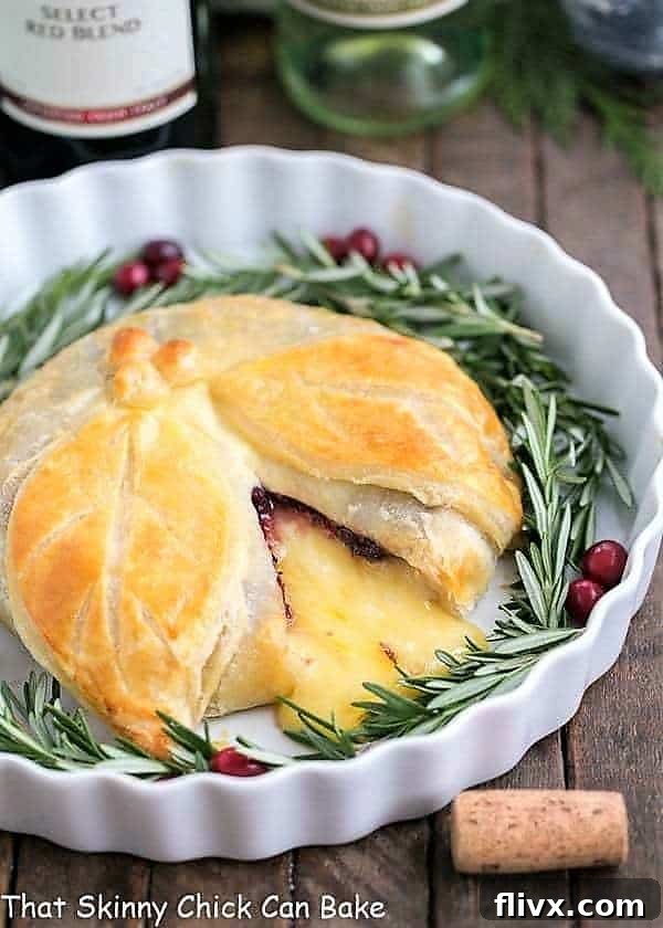 A stunning Cranberry Brie en Croute in a white ceramic dish, elegantly garnished with fresh rosemary sprigs and bright red cranberries, ready to be served as a holiday appetizer.