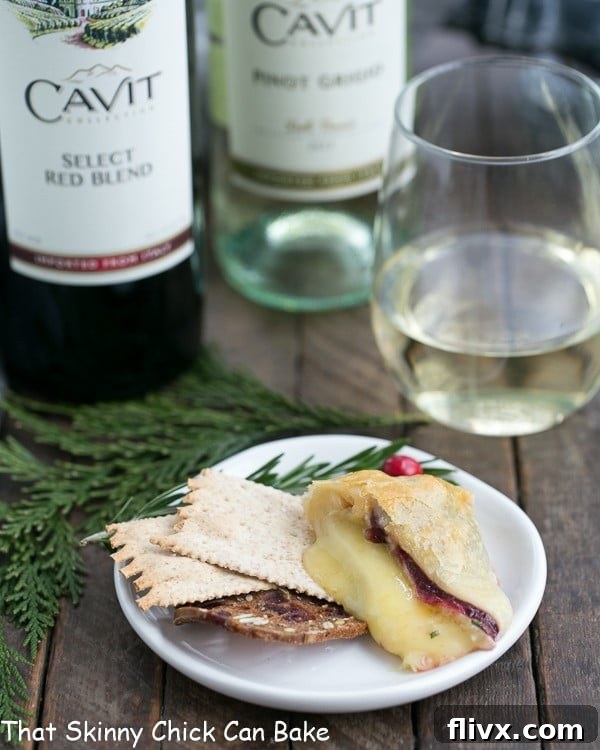A perfectly sliced piece of Cranberry Brie en Croute rests on a small white appetizer plate, accompanied by crisp crackers, showcasing its gooey center and flaky crust.