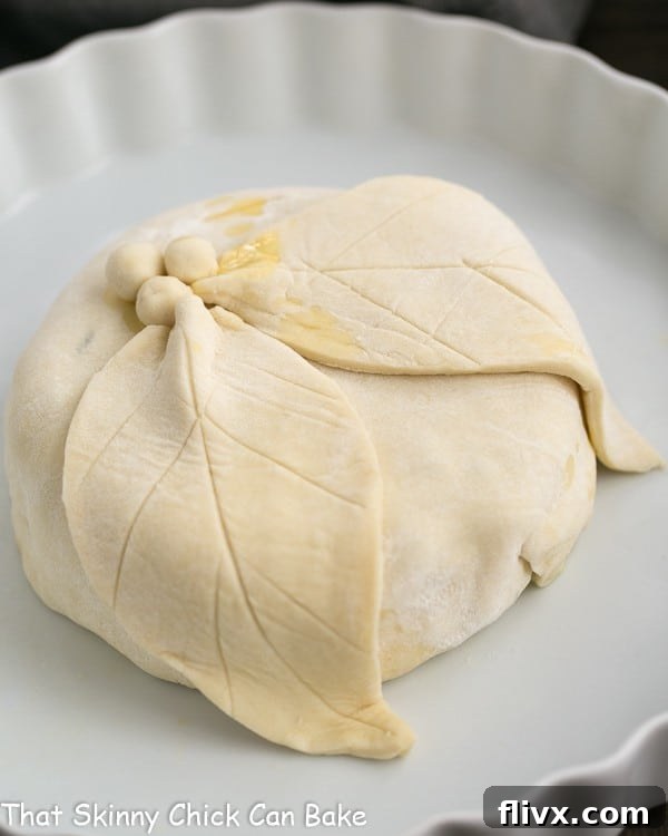 A pristine Cranberry Brie en Croute, meticulously wrapped in puff pastry and adorned with delicate pastry leaf decorations, waiting to be baked to golden perfection.