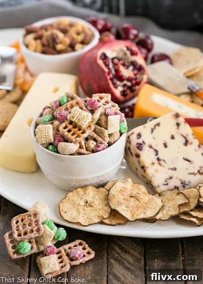 A bowl of festive White Chocolate Cashew Party Mix artfully placed on a rustic cheese and appetizer board with grapes and crackers