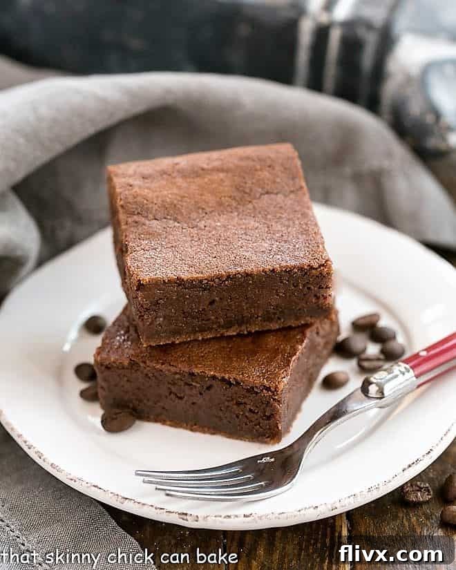 Rich Kahlua Brownies on a round white plate, surrounded by coffee beans, with a fork ready to dig in.