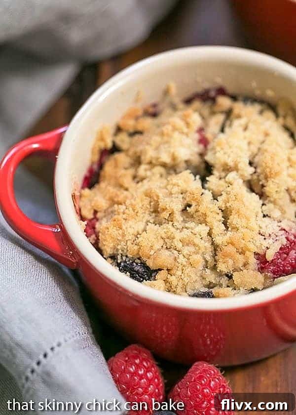 Overhead view of an Individual Berry Crisp in a vibrant red ceramic baking dish, ready to be served.